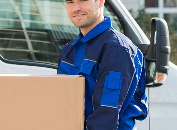 Portrait of happy delivery men carrying cardboard box while standing against truck