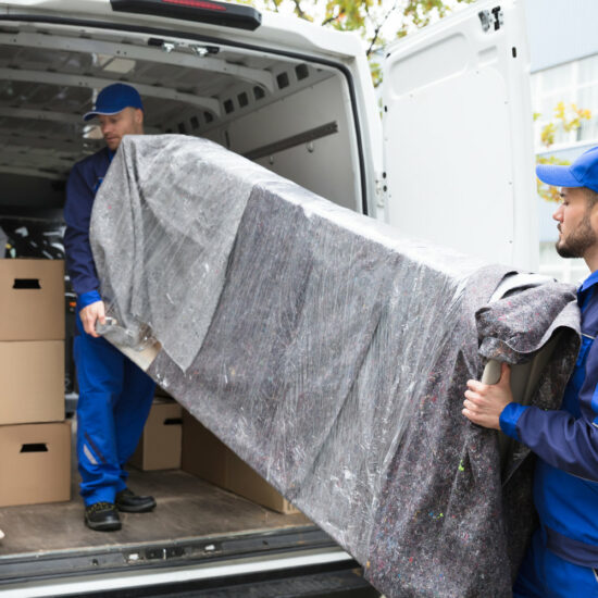 Two Young Delivery Men In Uniform Unloading Furniture From Vehicle
