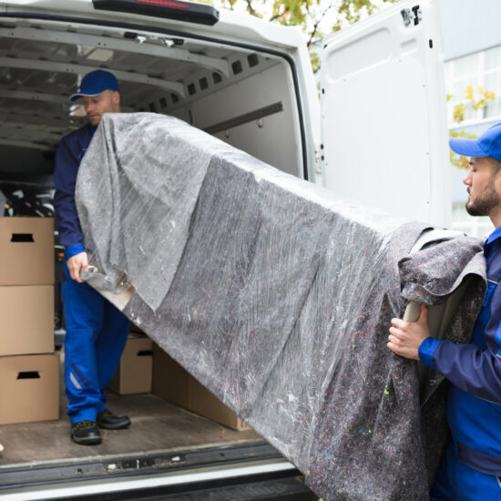 Two Delivery Men Unloading Furniture From Vehicle Two Young Delivery Men In Uniform Unloading Furniture From Vehicle