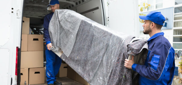 Two Young Delivery Men In Uniform Unloading Furniture From Vehicle